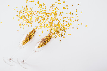 Glasses with golden confetti tinsel on white background. Flat lay, top view, copy space. Celebrate...