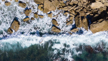 Aerial top view of waves breaking on rocks on a cliff in Spain