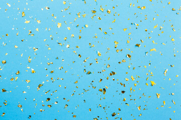 Gold confetti on blue paper background. Festive holiday backdrop. Birthday congratulations Christmas New Year. Flat lay, top view, copy space.