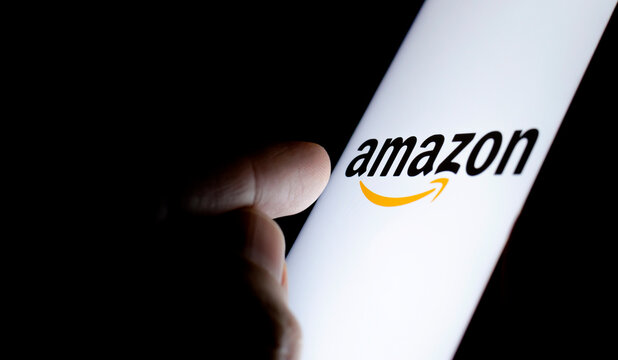 Amazon logo on a smartphone screen in a dark room and a finger pointing at it.