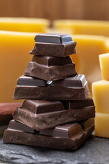 Tasty Swiss food, block of medium-hard yellow cheese emmental or emmentaler with round holes and high quality milk chocolate served in cubes as mountains top with Swiss flag.