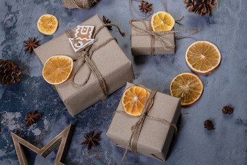 Wrapping rustic eco Christmas packages with brown paper, string and dries oranges on dark background