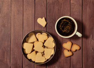 Heart shaped butter cookies in a tin box and on the table surface with a cup of coffee. Copy space.