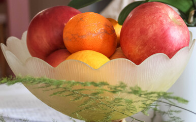Yellow glass bowl on a table full of fruits, apples, lemons and manadarins