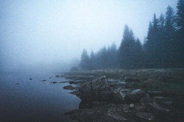 Coastal landscape of foggy lake. Stones in the water on foreground. Long exposure shot.