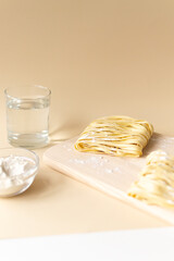 Natural homemade noodles with flour and a glass of water on a brown background. Vertical orientation. Copy space. Selective focus.