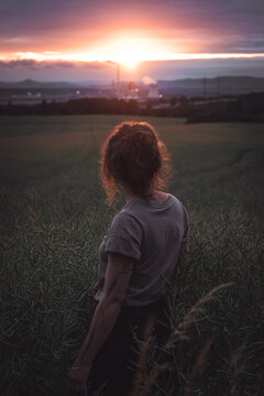 Young woman standing on a wheat field with sunrise on the background