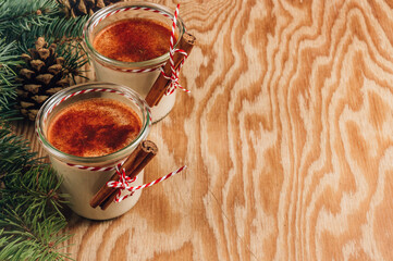 Traditional Christmas milk cocktail - Eggnog with cinnamon, served in two glasses on festive wooden table.