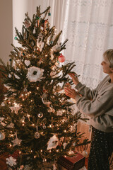 Young woman decorates Christmas tree. Holiday season. Lights, ornaments, vintage retro decor. Green fur tree. Merry Christmas, Happy New Year.Holiday is over. Pack stuff to the boxes. Red, green,white