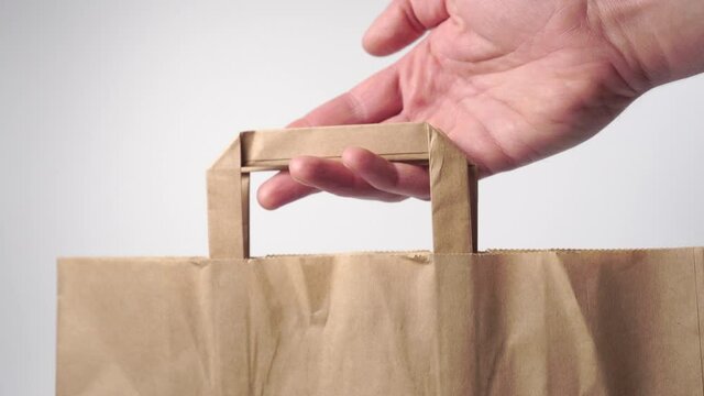 Hand gives a paper bag closeup on a white background. Shopping and discount concept