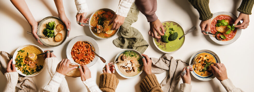 People Eating Autumn And Winter Creamy Vegan Soups, Fall And Winter Vegetarian Food Menu. Flat-lay Of Peoples Hands With Homemade Soup In Plates And Bread Slices Over White Table Background, Top View