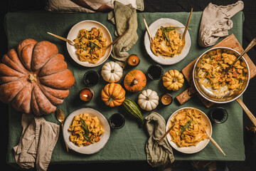 Flat-lay of Autumn dinner for gathering or Thanksgiving Day celebration party. Butternut squash pasta with sausage and sage in plates and red wine in glasses over linen tablecloth, top view