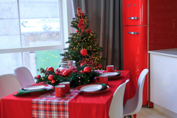 Interior light kitchen with red christmas decor. Preparing holiday dinner at home. Decorated new Year fir. Selective focus. Table with festive dishes, red refrigerator. Holidays table setting concept.