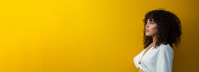 beautiful latin american young woman with curly hair looking to the left, on a yellow background