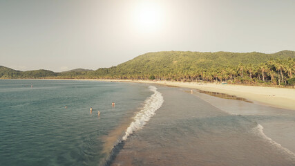 Sun over sand beach at sea coast aerial. Summer tropic paradise vacation at ocean bay. Nature landscape and seascape of El Nido Island, Philippines, Asia. Cinematic people relax at sunny day