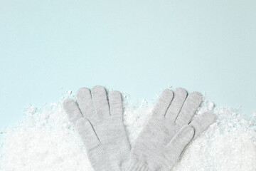 Stylish woolen gloves and artificial snow on light blue background, flat lay. Space for text