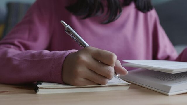 Hand of Asian women do homework, writing notebook, and Wear long sleeves while sitting in interior at home morning. Close up of young girl hand