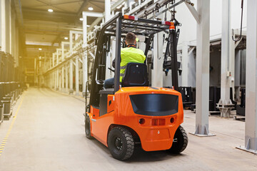 Storehouse employee in uniform working on forklift in modern automatic warehouse. Boxes are on the shelves of the warehouse. Warehousing, machinery concept. Logistics in stock.