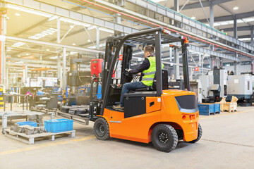 Storehouse employee in uniform working on forklift in modern automatic warehouse. Boxes are on the...