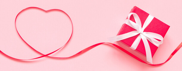 Heart shape made of red ribbon and red gift box with white bow on pink background. Card for Valentines, Mother, Women's day and 8 March. Copy space, mock up, banner