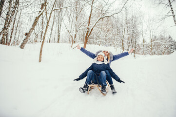 Beautiful mother in a blue jacket. Family sledding in a winter park. Little boy in a cute hat