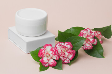 Beauty industry concept . White cosmetic cream jar top with flowers. Side view. Feminine hygienic skincare product on light pink background. Close-up.