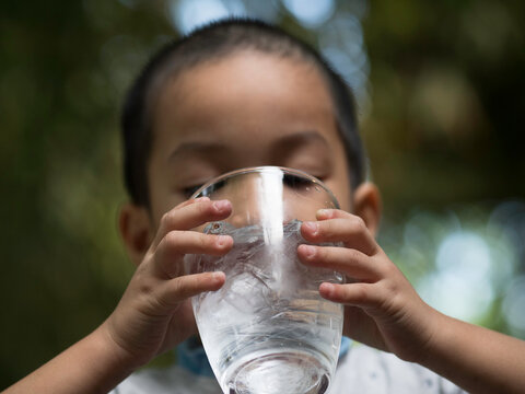 Asian kid drinking a glass of cold water.4 years old Asian boy holding water glass and drinking.