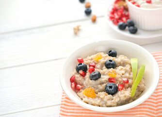Bowl of oatmeal porridge with pomegranate, blueberries apple and orange on rustic table, hot and healthy food for Breakfast. high fiber meal for good morning. selective focus