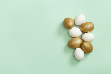Painted Easter eggs white and gold colored on light green paper. Minimal easter concept. Top view spring holiday background
