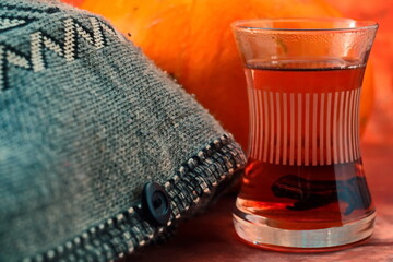 Traditional Turkish glass teacup of hot tea with dried peel of pomegranate in cup next grey soft warm thick knitted sweater on blurred yellow background. Selective focus