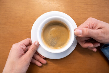 Female hands holding a cup of coffee on a wooden texture background