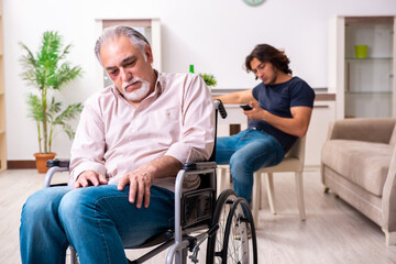 Old man in wheel-chair and young bad caregiver indoors