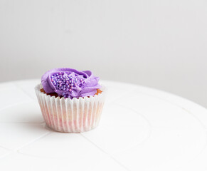 Vanilla cup cake with purple frosting and coloured sprinkles 