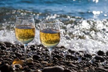 Two glasses of white wine or champagne stand on the rocks against the sea foam. concept of celebration or romantic date
