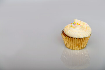 Vanilla cupcake with small multi colour ball sprinkles on a gold wrapper