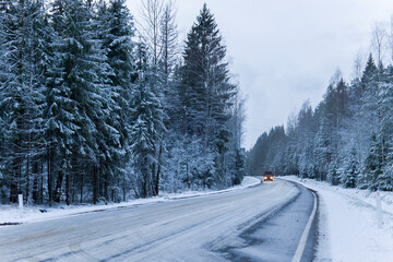 Car drives on empty snowy road in winter forest. Beautiful frosty white landscape at dawn.