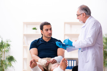 Fototapeta premium Young injured man visiting old doctor traumatologist
