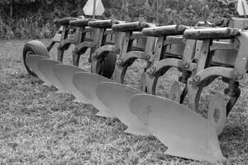 Grayscale close up view of a vintage tractor drawn mouldboard plough farm implement, used for plowing vertically through soil
