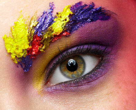 Close-up photo of female eye with unusual art make-up and face painting on brows and around eye
