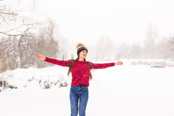 A young beautiful girl in a red sweater stands among the snowdrifts in the forest. Woman in red in a park winter when it snows.