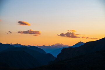 Colorful dawn landscape with beautiful mountains silhouettes and golden gradient sky with lilac clouds. Vivid mountain scenery with picturesque multicolor sunset. Scenic sunrise view to mountain range