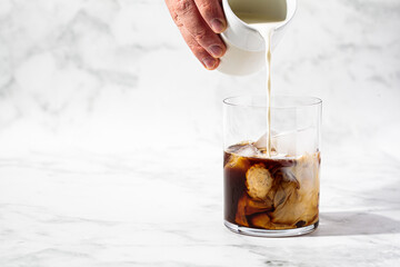 Cooking ice latte coffee. Hand pours milk into coffee glass, copy space. Summer drink concept.