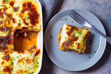 Portion of  Greek moussaka - potato and meat casserole with cheese on gray plate, dark background,...