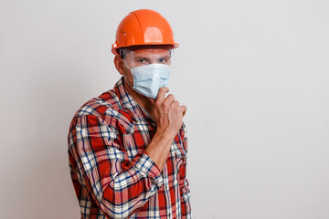 a man in a plaid shirt and an orange protective helmet on his head and wearing a medical mask on white background. mask mode. stop coronavirus