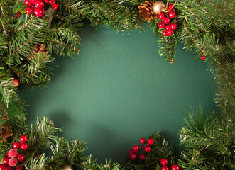 Christmas frame decoration with berries, cones and Christmas tree branch on the green background. Copy space.