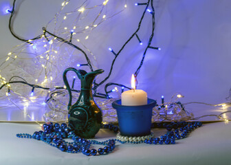 blue composition with candle and miniature mug, blue pearl ornaments in the foreground, white and...
