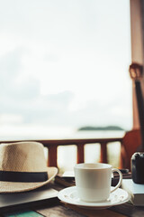Coffee, straw hat, camera and laptop on the table at resort and beach background.