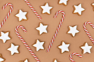 German star shaped glazed Christmas cookies called 'Zimtsterne' and candy canes on brown background