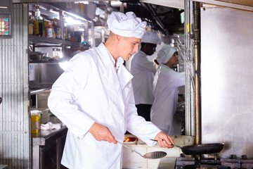 Fototapeta na wymiar Portrait of professional focused cook working with assistants in kitchen of restaurant