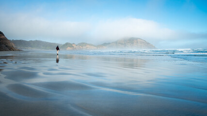 Fototapeta na wymiar A backpacker walking on the wet sandy beach with low clouds rolling in, Wharariki Beach, South Island, New Zealand